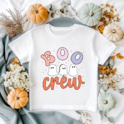 A white t-shirt with "Boo Crew" and ghost illustrations is surrounded by pumpkins, flowers, and leaves.