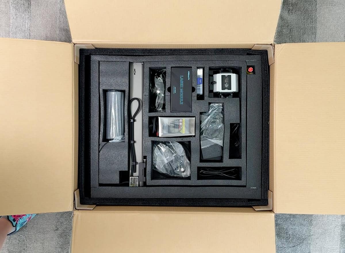 An open cardboard box showing a neatly packed collection of electronic equipment and accessories secured in black foam compartments.