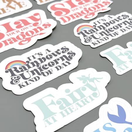A collection of whimsical stickers with motivational and fantasy-themed messages spread out on a flat surface.
