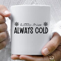 A person holds a white mug with the text "Little Miss Always Cold" between two snowflake icons.