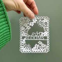 A person holding up a paper cut out that says love blooms.