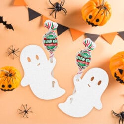 Two white ghost cutouts holding watermelon lollipops are surrounded by pumpkins, bats, and a triangular flag banner on an orange background.