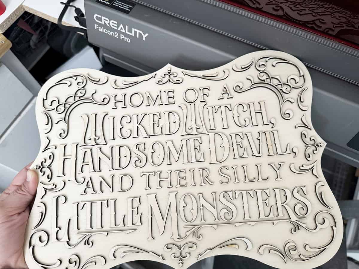 A carved wooden sign reads, "Home of a Wicked Witch, Handsome Devil, and their silly little monsters." The sign features ornate decorative elements.
