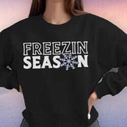 A person wearing a black sweatshirt with the words "FREEZIN SEASON," where the letter "O" is replaced with a snowflake.
