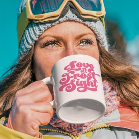 Person in winter gear drinks from a mug with "Love at Frost Sight" text.