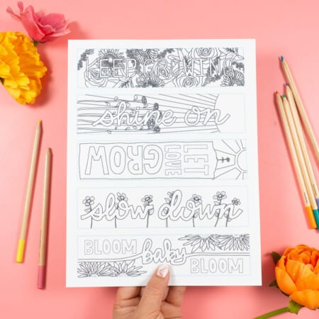Hand holding free floral bookmarks coloring page on pink background