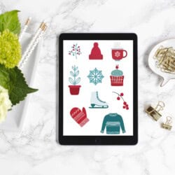 Tablet on marble table displaying winter-themed graphics: hat, mug, plant, snowflake, cupcake, mitten, sweater, skate, and berries. Nearby are pens, flowers, paper clips, and binder clips.