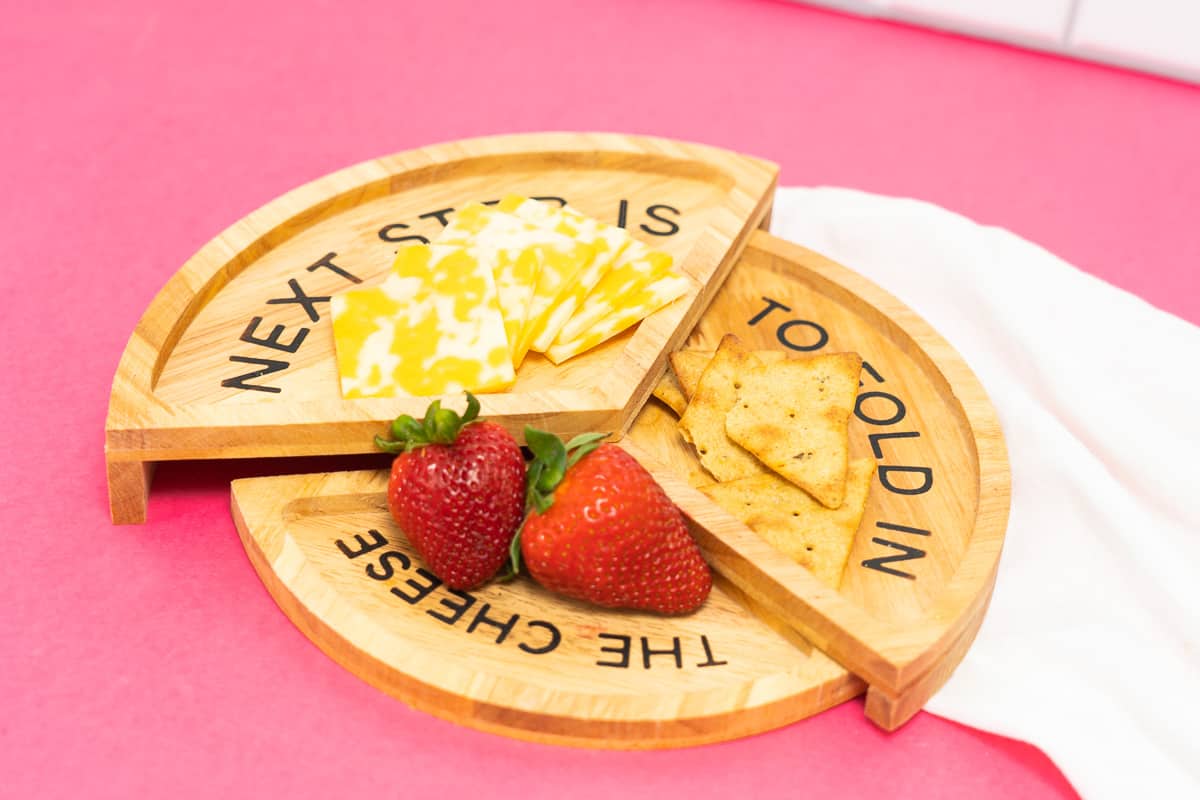 A wooden plate with cheese, crackers and strawberries.