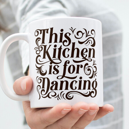 A person holding a white mug with the phrase "This Kitchen is for Dancing" printed in decorative black script.