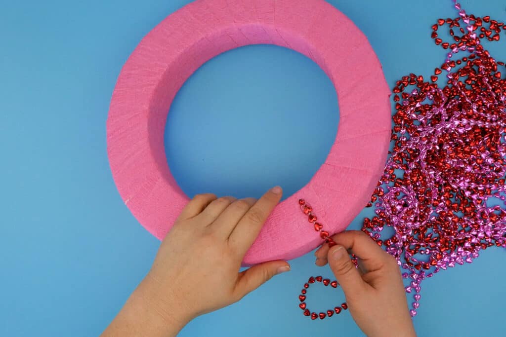 Hand gluing piece of metallic heart necklace to back of wreath