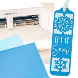 A Cricut machine next to blue paper and a blue bookmark with snowflake designs and the text "Let It Snow.